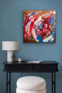 Abstract painting on a blue wall above a black console table with a lamp and books.