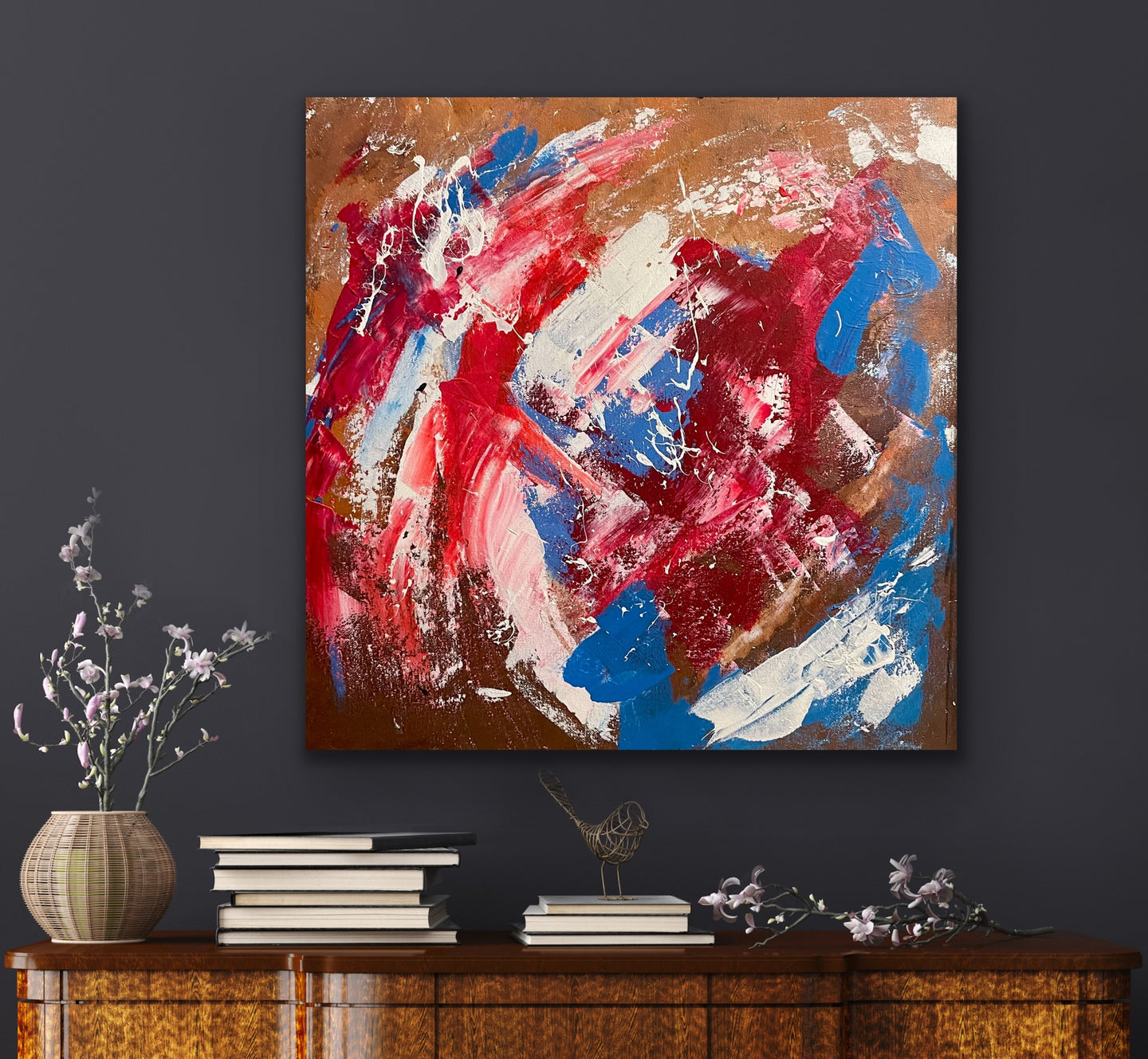 Abstract painting with red, blue, and white on a dark wall above a wooden cabinet.